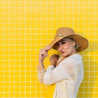 smiling senior woman holding her summer hat on a yellow tiled wall - fashion stock pictures, royalty-free photos & images
