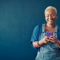 smiling woman in overalls texting on her phone against a blue background - fashion stock pictures, royalty-free photos & images