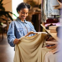 smiling woman looking at shirt while shopping in a clothing store - fashion stock pictures, royalty-free photos & images
