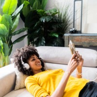 smiling woman lying on couch with cell phone and headphones - home decoration stock pictures, royalty-free photos & images