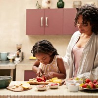 smiling woman standing by daughter cutting strawberry - home decoration stock-fotos und bilder