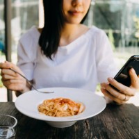 smiling woman using her mobile phone while having meal at a cafe outdoors - junk food stockfoto's en -beelden