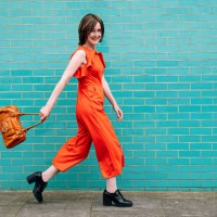 smiling woman wearing jumpsuit walking by brick wall - fashion stock pictures, royalty-free photos & images