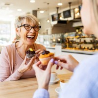 smiling women talking over cupcake and coffee - food stockfoto's en -beelden