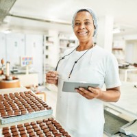 smiling worker using a digital tablet in a commercial chocolate making factory - food stock pictures, royalty-free photos & images