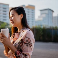 smiling young asian woman enjoying a take away coffee in the morning - junk food stock pictures, royalty-free photos & images