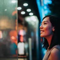 smiling young asian woman standing in front of a boutique and looking at shop window, shopping in city in the evening, with colourful neon lighting reflected on her - fashion stock pictures, royalty-free photos & images