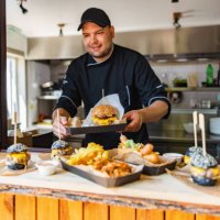 smiling young caucasian chef carring a tray with a delicious big meat burger at a small fast-food restaurant - junk food stock pictures, royalty-free photos & images