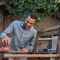 smiling young man sanding a chair outdoors - home decoration stock pictures, royalty-free photos & images