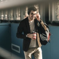 smiling young man with headphones, cell phone and takeaway coffee walking at the station - junk food stock pictures, royalty-free photos & images
