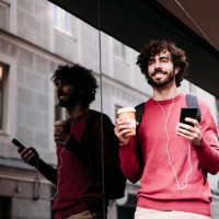smiling young man with smart phone and coffee cup standing at footpath - junk food stock pictures, royalty-free photos & images