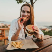 smiling young woman eating burger and fries during summer vacation in greece - junk food stock pictures, royalty-free photos & images