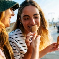 smiling young woman feeding ice cream to sister while spending enjoying in city - food stockfoto's en -beelden