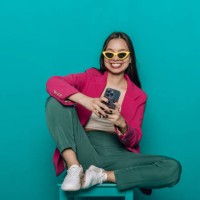 smiling young woman sitting on a chair chatting in via smartphone using the internet. - fashion stock pictures, royalty-free photos & images