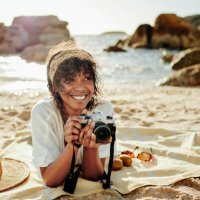 smiling young woman taking photos while relaxing on a sandy beach - travel stock pictures, royalty-free photos & images
