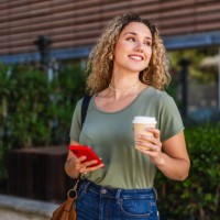 smiling young woman walking with coffee and smartphone in city - junk food stock pictures, royalty-free photos & images