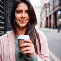 smiling young woman with disposable coffee cup standing by shutter in city - junk food stock pictures, royalty-free photos & images