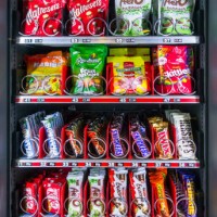 Snack vending machine / snack dispenser selling colourful sweets and chocolate bars in public place.