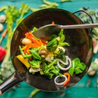 stir frying and sauteing a variety of fresh colorful market vegetables in a hot steaming wok with vegetables on on a turquoise colored wood table background below the wok. - food stock pictures, royalty-free photos & images