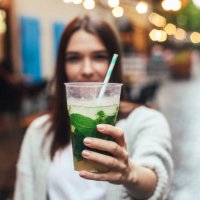 street portrait of young woman holding a glass of mojito in hands. blurred restaurant in background. summer lifestyle, drinks concept. - junk food stock pictures, royalty-free photos & images