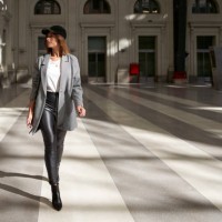 stylish woman wearing white t-shirt, long blazer, black leather pants and black cap walking alone through a public corridor. - fashion photos et images de collection