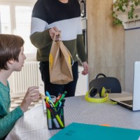 surprised boy looking at paper bag with food delivery in his father's hand - junk food stock pictures, royalty-free photos & images