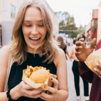 surprised young woman holding burger next to male friend at food festival - junk food stock pictures, royalty-free photos & images
