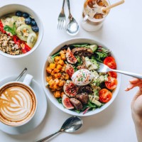 table top view of a woman eating healthy beef cobb salad bowl with greens, avocado, cherry tomatoes, figs, pumpkin and soft boiled egg, vegan chia and quinoa granola fruit bowl and coffee by the side. healthy food trend. nutr