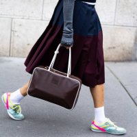 Tamu Mcpherson wears a blue sweater, a grey and dark grey jacket, grey long gloves, a blue and bordeaux pleated maxi skirt, a brown leather Miu Miu...