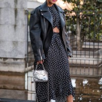 Tamu Mcpherson wears black and white polka dot dress, black leather jacket, blue sunglasses, silver Stella McCartney bag, black sandals, outside...