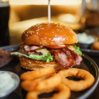 tasty beef burger with bacon, lettuce, cheese and tomato, onion rings, garlic sauce and a glass of beer - food stock pictures, royalty-free photos & images