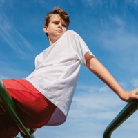 teen boy in sports wear outdoors sits on bars against blue sky - fashion stock pictures, royalty-free photos & images