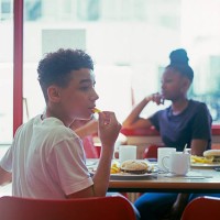 teenage boy in cafe eating burger and chips - junk food stockfoto's en -beelden
