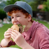 teenage boy with baseball cap eating hamburger - junk food stock pictures, royalty-free photos & images