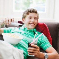 teenage boy with snacks holding remote control - junk food stockfoto's en -beelden