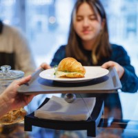 teenage girl in plaid shirt taking croissant sandwich on the counter in cafeteria - junk food stock pictures, royalty-free photos & images