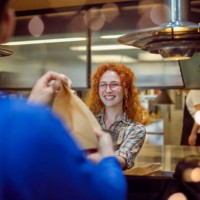 the cheerful waitress has prepared the delivery orders and gives them to the delivery man. - junk food stock pictures, royalty-free photos & images