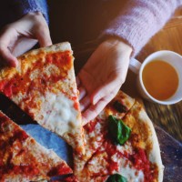 the girl takes a piece of vegetarian pizza with mozzarella cheese, tomatoes, spices and fresh basil. delicious italian food. sliced pizza margarita on a wooden board. close up. delicious lunch, snack - junk food stock picture