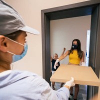 the new normal. food delivery at home and coronavirus protection. young teenager and her little sister receiving pizza delivery at home and paying for it. illness prevention during covid-19 pandemic. people with protective ma