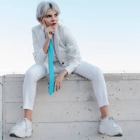 thoughtful young woman wearing white suit sitting on retaining wall against clear sky - fashion stock-fotos und bilder