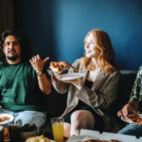 three cheerful gen z friends sitting on sofa in cozy room eating pizza and talking - junk food stock pictures, royalty-free photos & images