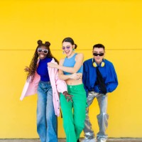 three fashionable young adults are posing and smiling against a vibrant yellow wall, showcasing their unique style - fashion stock pictures, royalty-free photos & images
