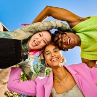 three gen z adults forming a circle with their arms and smiling outdoors in an urban environment. low angle shot. - fashion stock pictures, royalty-free photos & images