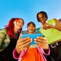 three gen z friends using a smartphone together. low angle shot with modern buildings in the background. social media and friendship concept. - fashion stock pictures, royalty-free photos & images