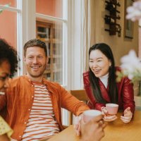 three young people sit around a table and giggle as they have a lighthearted discussion and drink coffee / tea - coffee stock pictures, royalty-free photos & images