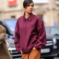Tina Kunakey wears a burgundy oversized bomber jacket, brown suede flared pants , white sneakers shoes, outside Miu Miu , during the Womenswear...