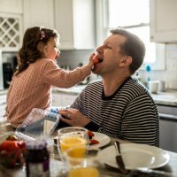 toddler girl feeding her father a strawberry in kitchen - food stock pictures, royalty-free photos & images