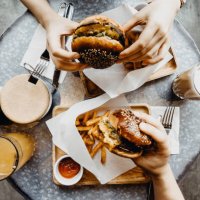 top view of friends having a good time eating burgers with french fries and drinks in a cafe - junk food stock pictures, royalty-free photos & images
