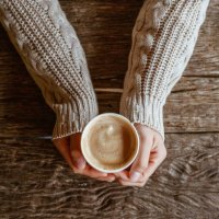 top view of woman hands holding a cup of hot milk coffee before drinking on wooden table. - coffee stock pictures, royalty-free photos & images