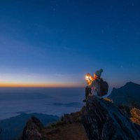 tourist woman holding a lantern while sitting on the rock on top of doi pha tang mountain a high cliff over the thai-laotian border located in wiang kaen district of chiang rai province of thailand. beautiful view before the 